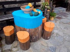 an outdoor table made out of logs and painted blue with orange accents, in front of a bench