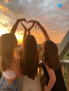 three girls standing on a balcony with their arms in the air making a heart shape