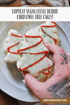 someone is holding up some christmas tree cookies on a white plate with red and green sprinkles