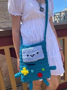 a woman is holding a crocheted bag with a monster on it's side