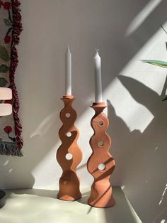 two candles sitting next to each other in front of a wall with a rug on it