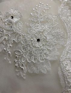 closeup of white fabric with beading and flowers on the bottom, as seen from above