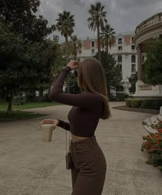 a woman standing in front of a building holding a cup and looking into the distance