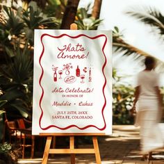 a white sign sitting on top of a wooden easel in front of palm trees