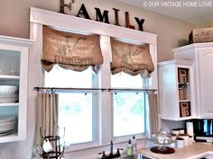 a kitchen with white cabinets and windows covered in burlocked roman shade valances