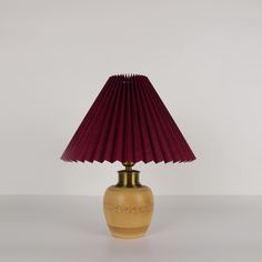 a lamp with a red shade on it sitting on top of a white table next to a wall