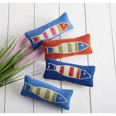 three colorful fish pillows sitting on top of a white wooden floor next to some grass