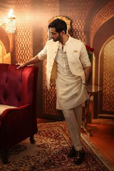 a man standing next to a red chair in front of a gold and white wall