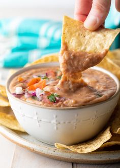 a hand dipping a tortilla chip into a bowl of salsa