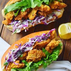 two chicken sandwiches with lettuce and coleslaw on a wooden table next to a lemon wedge