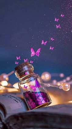 an open book with pink and purple butterflies flying out of it, in front of a string of fairy lights