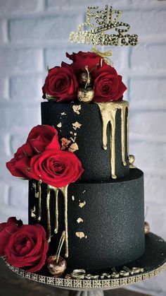 a three tiered black cake with red roses on the top and gold drips