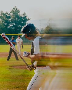 a man holding a baseball bat on top of a field with other people in the background