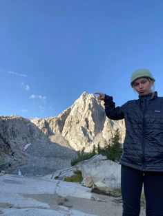 a woman standing on top of a mountain pointing to the sky