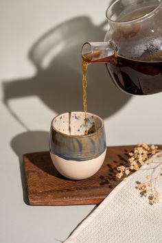 tea being poured into a cup on top of a wooden tray