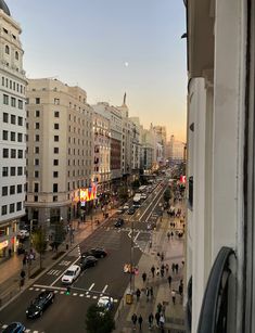 a city street filled with lots of traffic next to tall buildings and people walking on the sidewalk