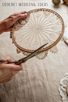 two hands are holding a piece of lace and scissors on a table with doily