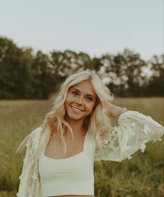 a woman standing in a field with her arms behind her head and smiling at the camera