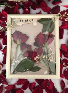 some red roses and white flowers in a frame on the ground with petals around them