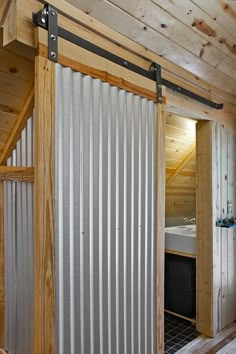 an open door leading to a bathroom with a bed in the corner and wooden walls