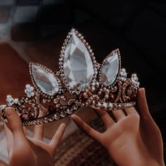 a woman's hand holding a tiara in front of her face, with other hands on the ground