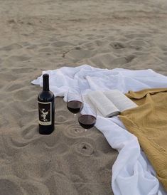 a bottle of wine sitting on top of a beach next to a glass of wine