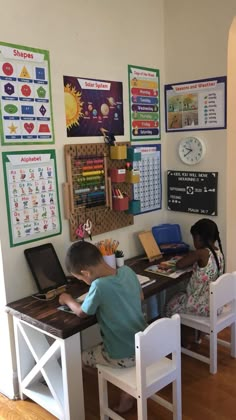 two children are sitting at a desk in front of a wall with posters on it