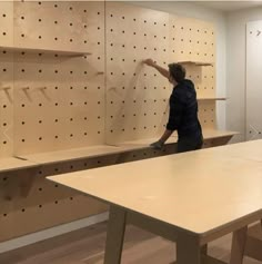 a man is working on some shelves in a room with pegboard walls and wooden tables