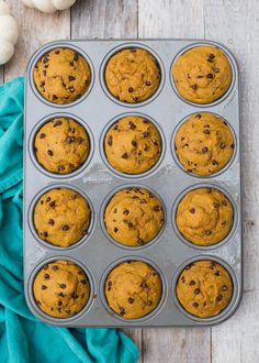 a muffin tin filled with pumpkin chocolate chip muffins on top of a wooden table