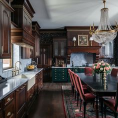 a large kitchen with wooden cabinets and chandelier hanging from the ceiling, along with red chairs