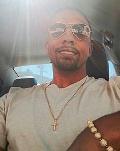 a man wearing sunglasses sitting in the back seat of a car with a cross necklace on his neck