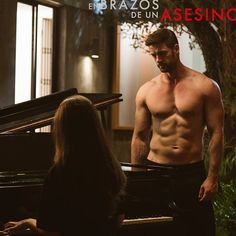 a shirtless man standing next to a piano in front of a woman with long hair