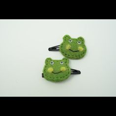 two green felt hair clips with faces drawn on them