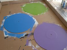 three different colored discs sitting on top of a cardboard box with paint splattered all over them