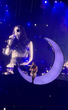 a woman sitting on top of a crescent moon in front of a stage with lights