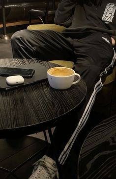 a man sitting at a table with a cup of coffee and cell phone on it