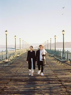 two women walking on a pier with benches in the background