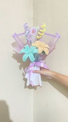 a hand holding a bouquet of flowers with ribbons on the top and bottom, in front of a white wall