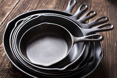 a stack of black pots and pans sitting on top of a wooden table with utensils