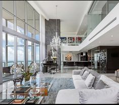 a large living room filled with furniture next to tall glass walls and floor to ceiling windows