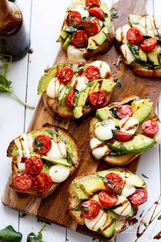 several open faced sandwiches with tomatoes, avocado and cheese on a wooden cutting board