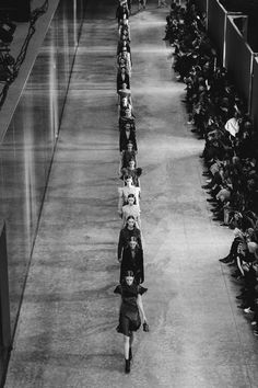 a black and white photo of people walking down a runway in front of an audience