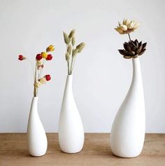 three white vases with flowers in them on a table