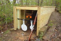 a wooden outhouse in the woods with two white pans hanging from it's roof