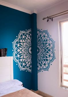 a bed sitting under a window next to a wall painted with blue and white designs