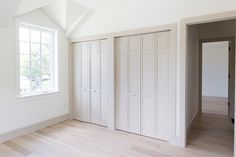 an empty room with white closets and wood flooring in front of a large window