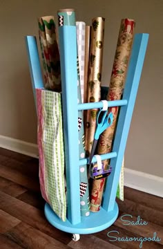 a blue holder with rolls of wrapping paper and scissors in it on a wooden floor