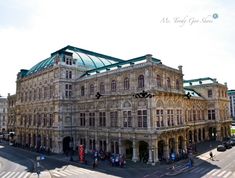 an old building with a green roof and people walking around in the street below it