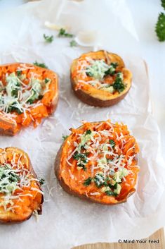 four baked sweet potatoes with cheese and herbs on top, sitting on waxed paper