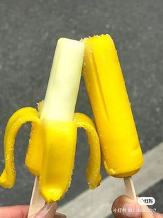 a person holding two popsicles with yellow icing on them and one has a banana peel sticking out of it